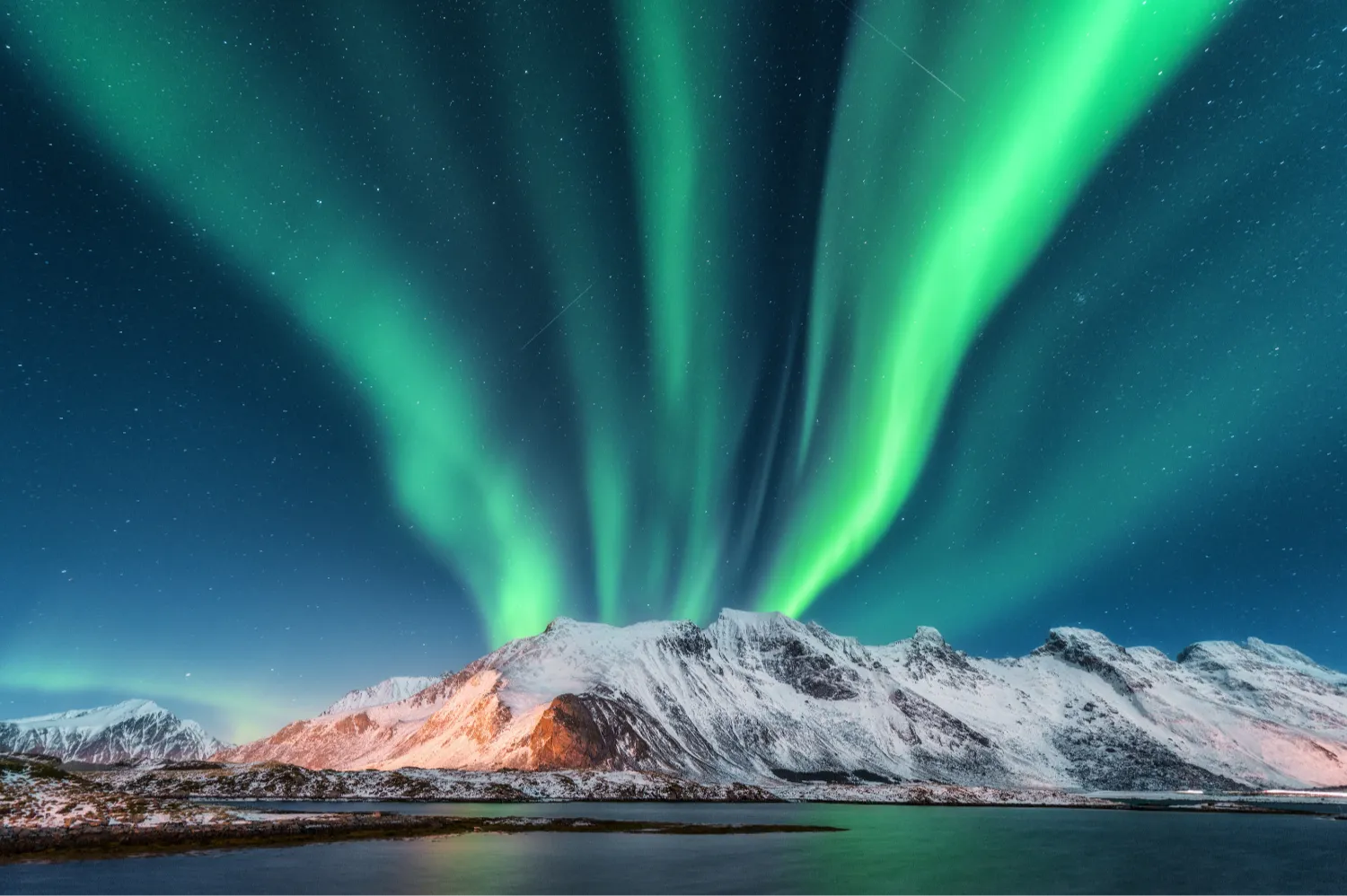 Green Northern Lights in Norway dance over snowy mountains reflected in a calm lake, under a starry night sky, creating a serene and magical scene.